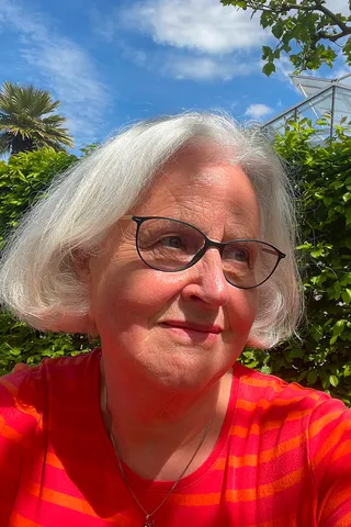 Ilka Scholz mit grauem Bob und Brille in einem sonnigen Garten.